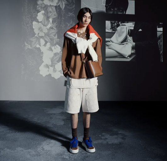 A man wearing a Denim Tears outfit with a brown jacket and white shorts