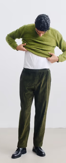 A man wearing A Kind of Guise green wool sweatshirt and a green corduroy pants with black shoes