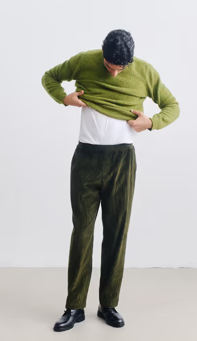 A man wearing A Kind of Guise green wool sweatshirt and a green corduroy pants with black shoes