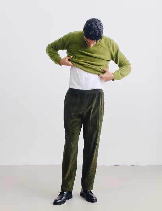 A man wearing A Kind of Guise green wool sweatshirt and a green corduroy pants with black shoes