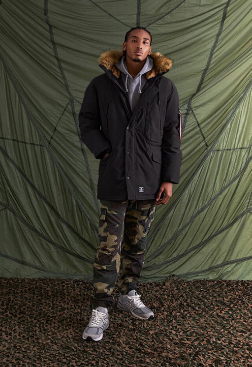 A man wearing an Alpha Industries jacket and camo pants