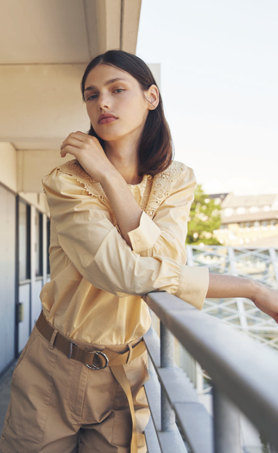 A woman wearing a Minimum light yellow button up and brown pants
