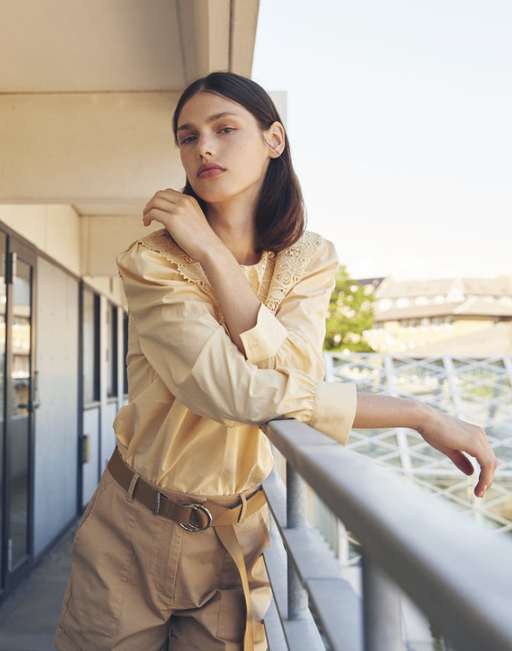 A woman wearing a Minimum light yellow button up and brown pants