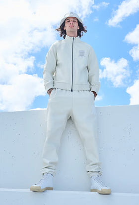 A man wearing a Avirex light grey track suit and bucket hat