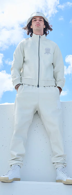 A man wearing a Avirex light grey track suit and bucket hat