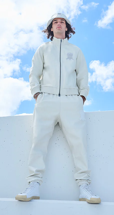 A man wearing a Avirex light grey track suit and bucket hat