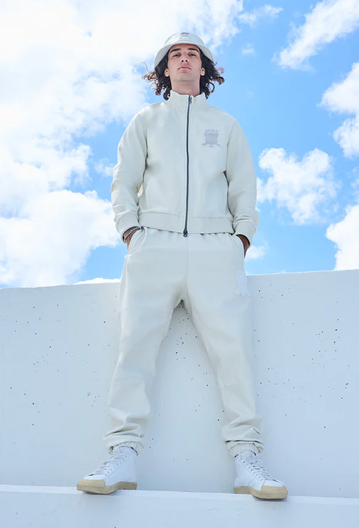 A man wearing a Avirex light grey track suit and bucket hat