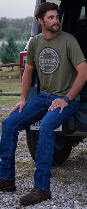 A man wearing a pair of black Chippewa Boots with blue jeans and a green shirt