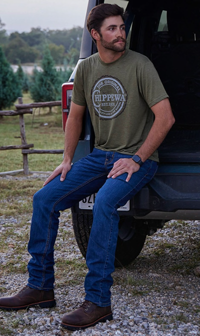 A man wearing a pair of black Chippewa Boots with blue jeans and a green shirt