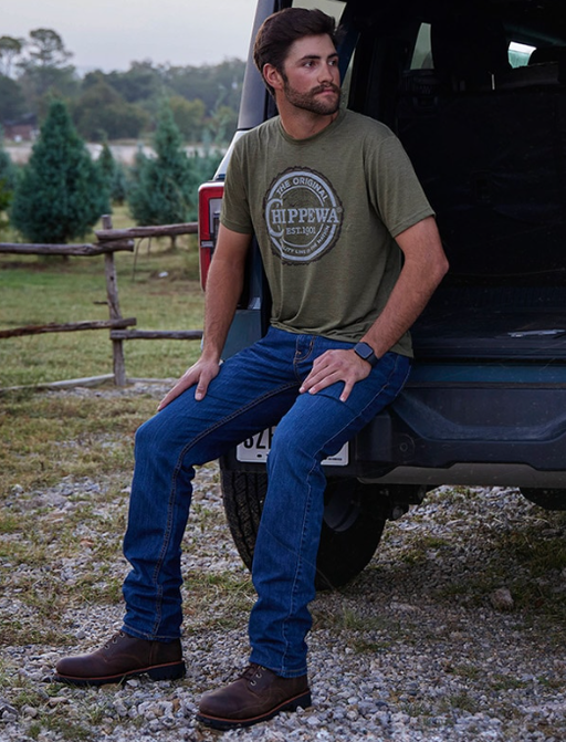 A man wearing a pair of black Chippewa Boots with blue jeans and a green shirt