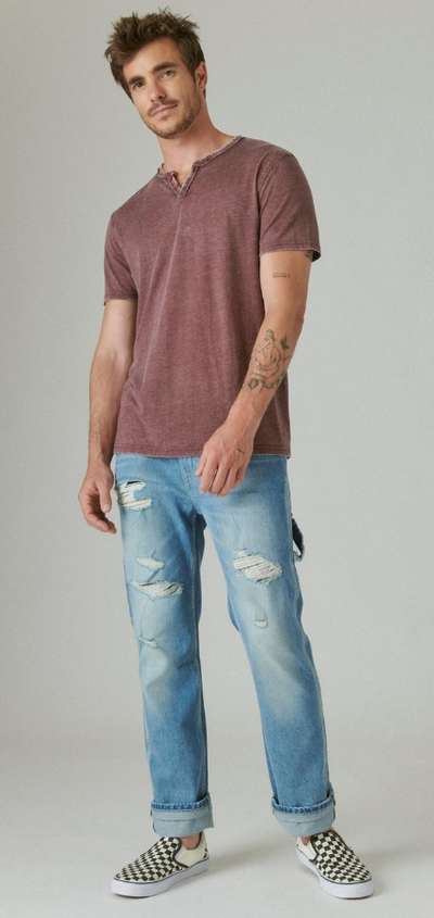 A man wearing a red-washed Lucky Brand t-shirt and blue jeans