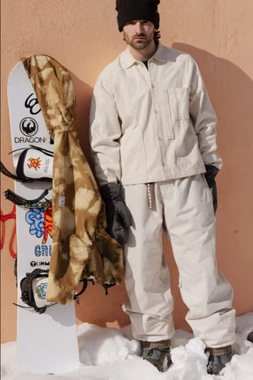 A man wearing a brown camo print 686 snowboard jacket with black gloves and beanie