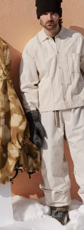 A man wearing a brown camo print 686 snowboard jacket with black gloves and beanie