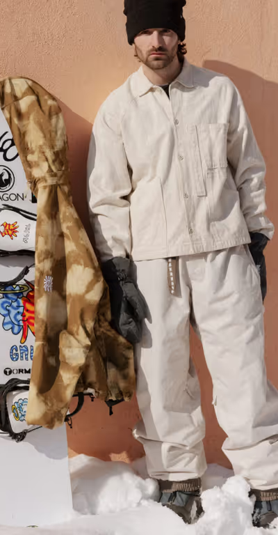 A man wearing a brown camo print 686 snowboard jacket with black gloves and beanie