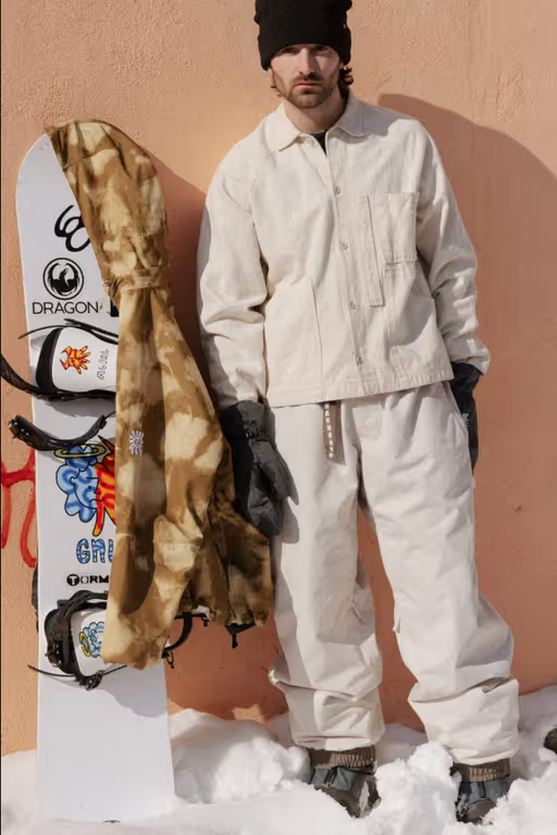 A man wearing a brown camo print 686 snowboard jacket with black gloves and beanie
