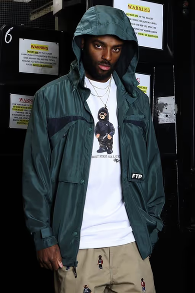 A man wearing a FTP outfit featuring a white t-shirt and blue rain coat