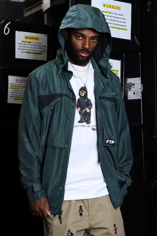 A man wearing a FTP outfit featuring a white t-shirt and blue rain coat