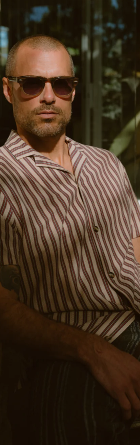 A man wearing a Barton Perreira striped shirt in red and white along with sunglasses
