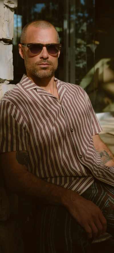 A man wearing a Barton Perreira striped shirt in red and white along with sunglasses
