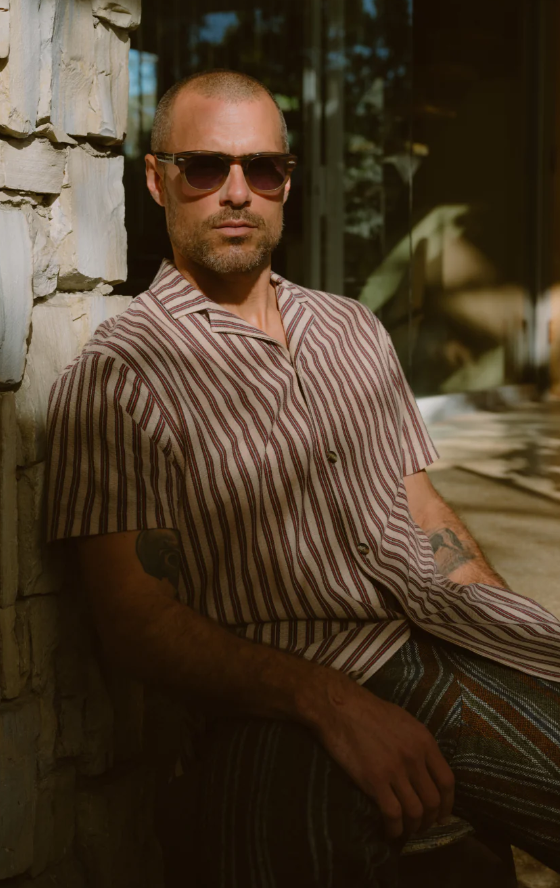 A man wearing a Barton Perreira striped shirt in red and white along with sunglasses