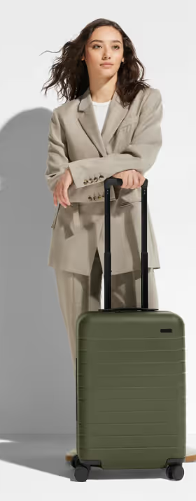 A woman holding an olive green Away suitcase