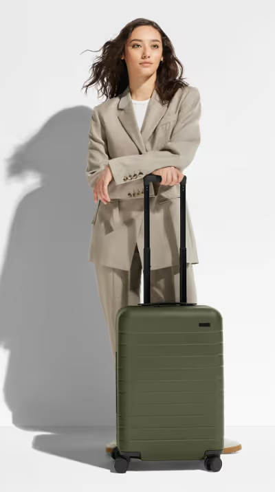 A woman holding an olive green Away suitcase