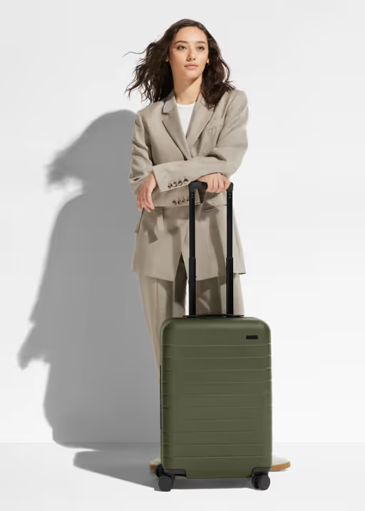 A woman holding an olive green Away suitcase