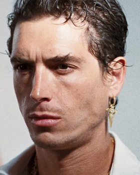 A man wearing a In Gold We Trust Paris earring " cross pendant " - gld