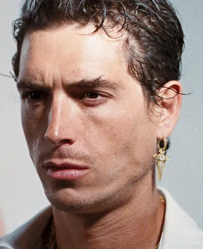 A man wearing a In Gold We Trust Paris earring " cross pendant " - gld
