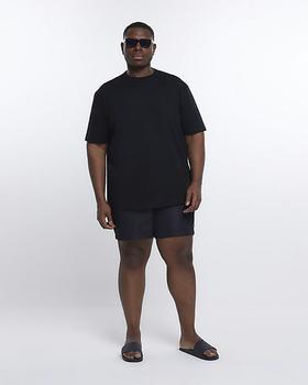 A man wearing a River Island Plus black t-shirt with black swim trunks