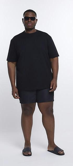 A man wearing a River Island Plus black t-shirt with black swim trunks