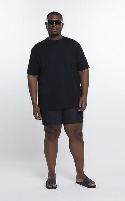 A man wearing a River Island Plus black t-shirt with black swim trunks