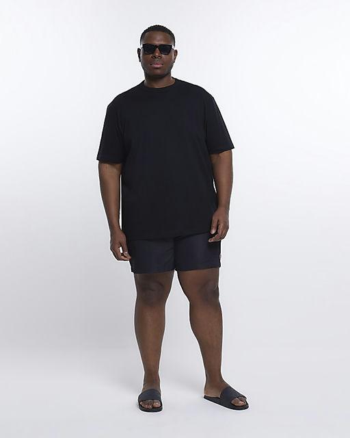 A man wearing a River Island Plus black t-shirt with black swim trunks