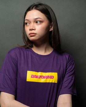 A woman wearing a Team Manila daily grind dg logo bar tshirt purple