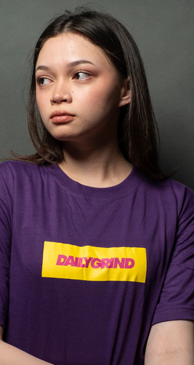 A woman wearing a Team Manila daily grind dg logo bar tshirt purple