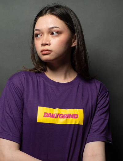 A woman wearing a Team Manila daily grind dg logo bar tshirt purple