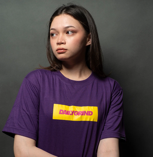 A woman wearing a Team Manila daily grind dg logo bar tshirt purple