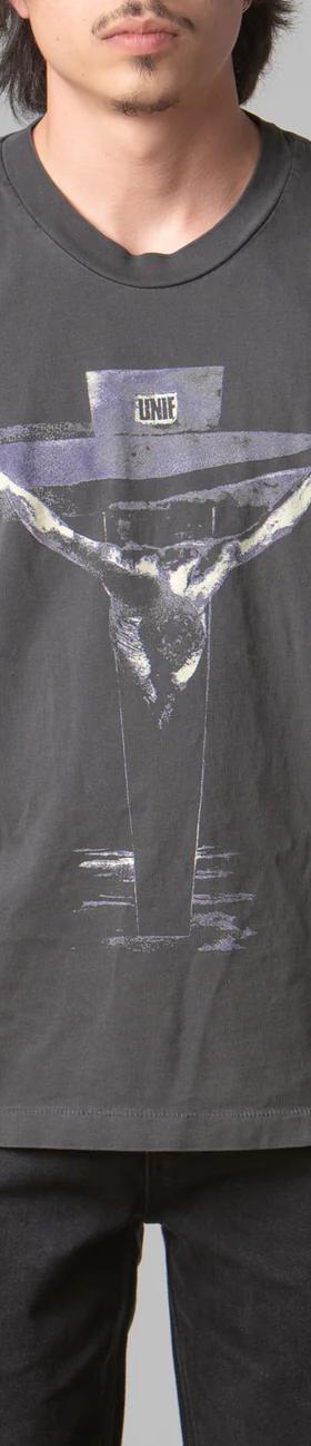 A man wearing a black UNIF t-shirt featuring a cross with black pants