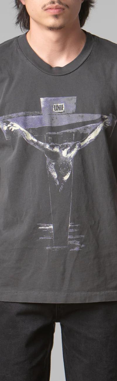 A man wearing a black UNIF t-shirt featuring a cross with black pants