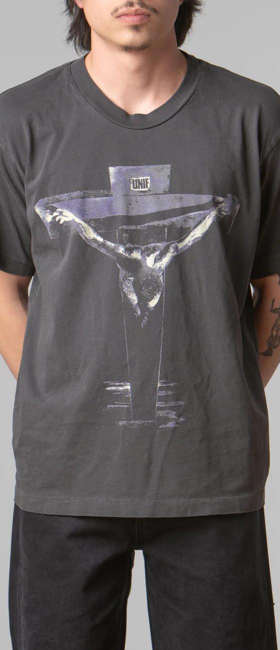 A man wearing a black UNIF t-shirt featuring a cross with black pants