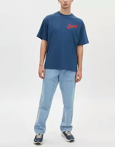 A man wearing Coach dark denim boardwalk specials t shirt in organic cotton