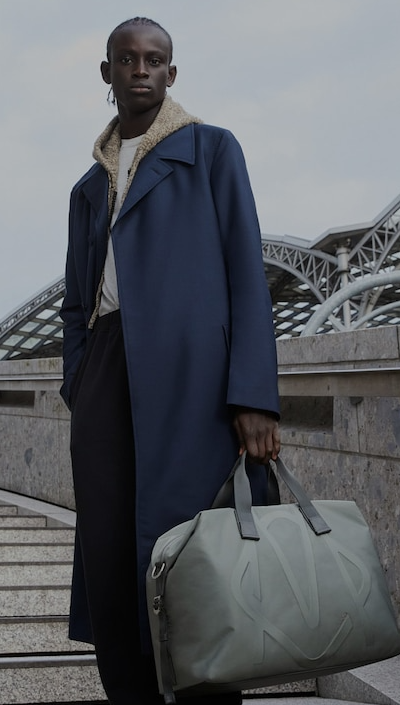 A man holding a Rimowa grey bag and a blue trench coat