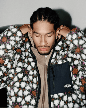 A man wearing a white and brown Stussy fleece with a brown jacket underneath