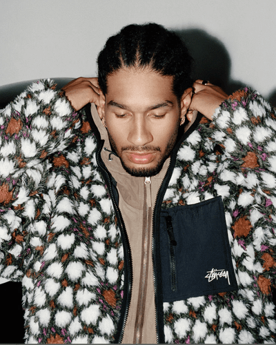 A man wearing a white and brown Stussy fleece with a brown jacket underneath