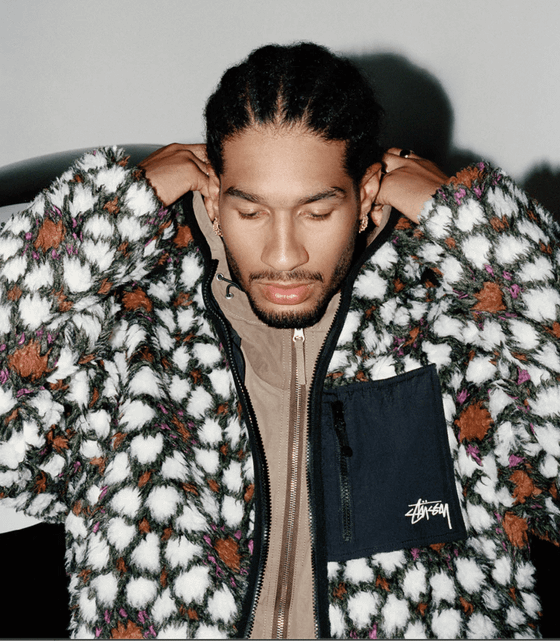 A man wearing a white and brown Stussy fleece with a brown jacket underneath