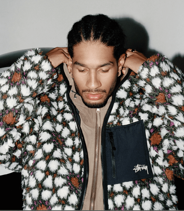 A man wearing a white and brown Stussy fleece with a brown jacket underneath