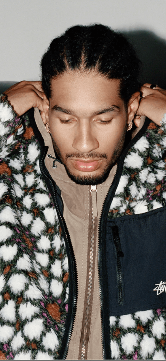 A man wearing a white and brown Stussy fleece with a brown jacket underneath