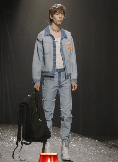 A man on a fashion runway wearing a Maison Margiela denim jacket and matching pants along with a white high-heel boots