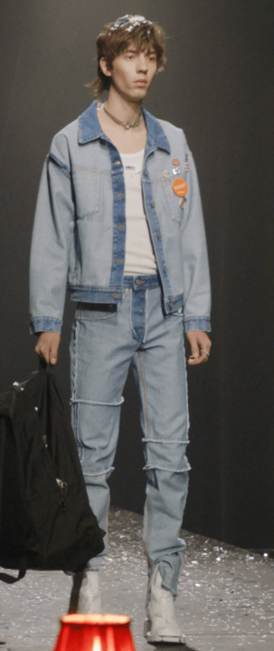 A man on a fashion runway wearing a Maison Margiela denim jacket and matching pants along with a white high-heel boots