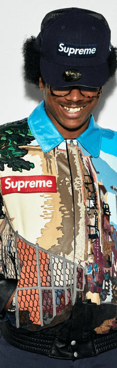 A man wearing a Supreme NYC style colorful graphic coaches jacket with a supreme box logo hat